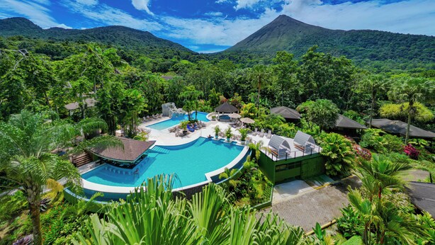 A resort with multiple swimming pools surrounded by lush greenery and a mountain in the background.