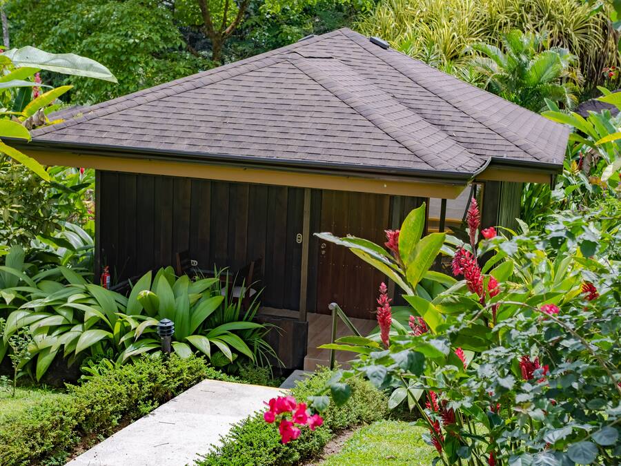 A small, single-story building with a sloped roof, surrounded by lush greenery and tropical plants.