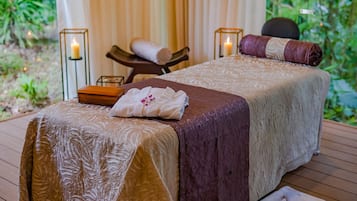 Ein Spa-Raum mit zwei Betten, jeweils mit einer Decke unterschiedlicher Textur, und einer Holzbank mit einem Handtuch.