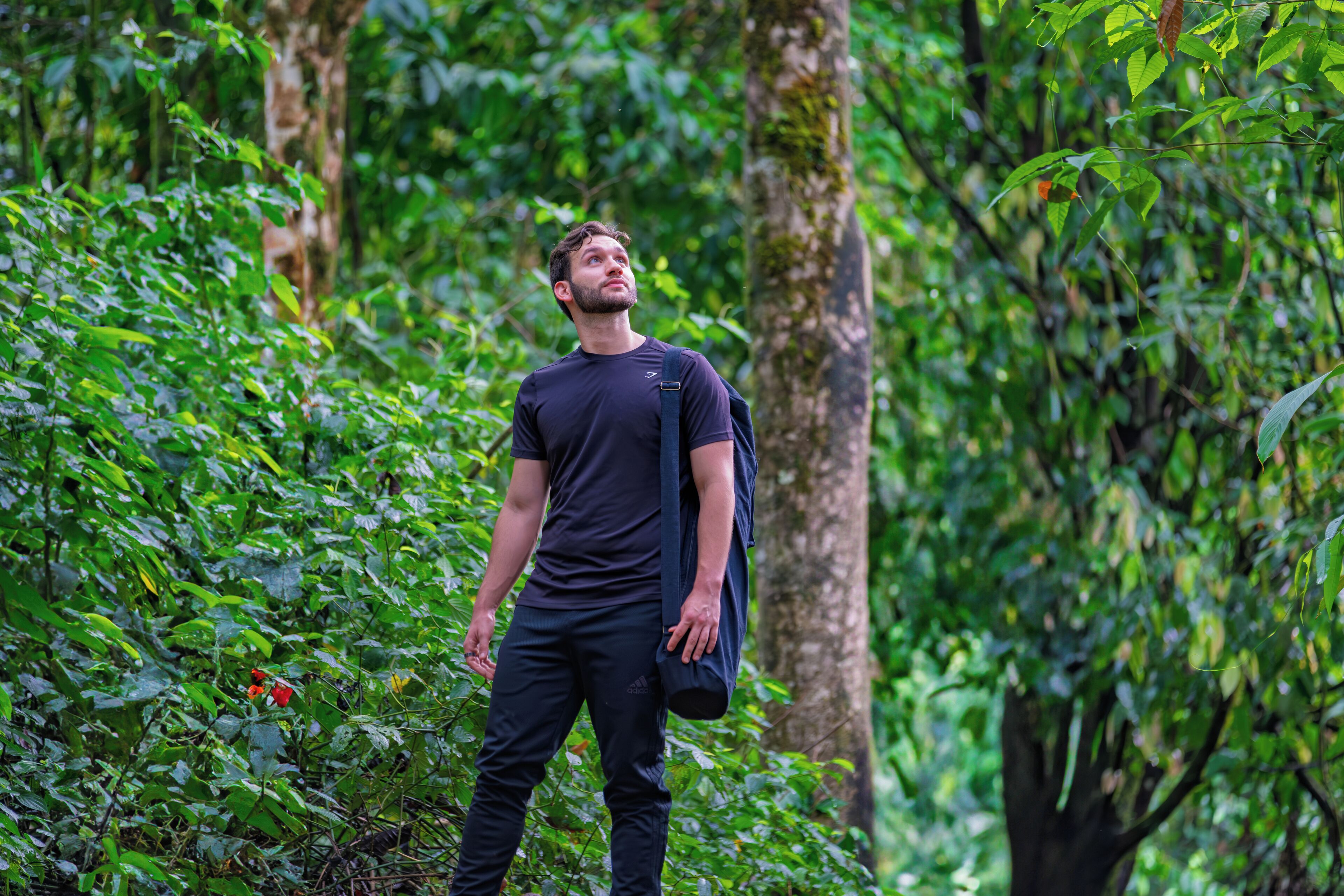 A person standing in a forested area with dense green foliage and trees.