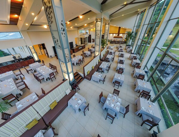 A spacious restaurant with multiple dining areas, large windows, and a modern interior design. - Hotel Lomas del Volcán (La Fortuna)