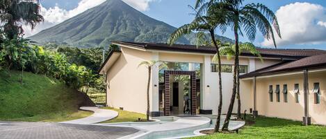A modern house with a curved driveway, palm trees, and a mountain in the background.
