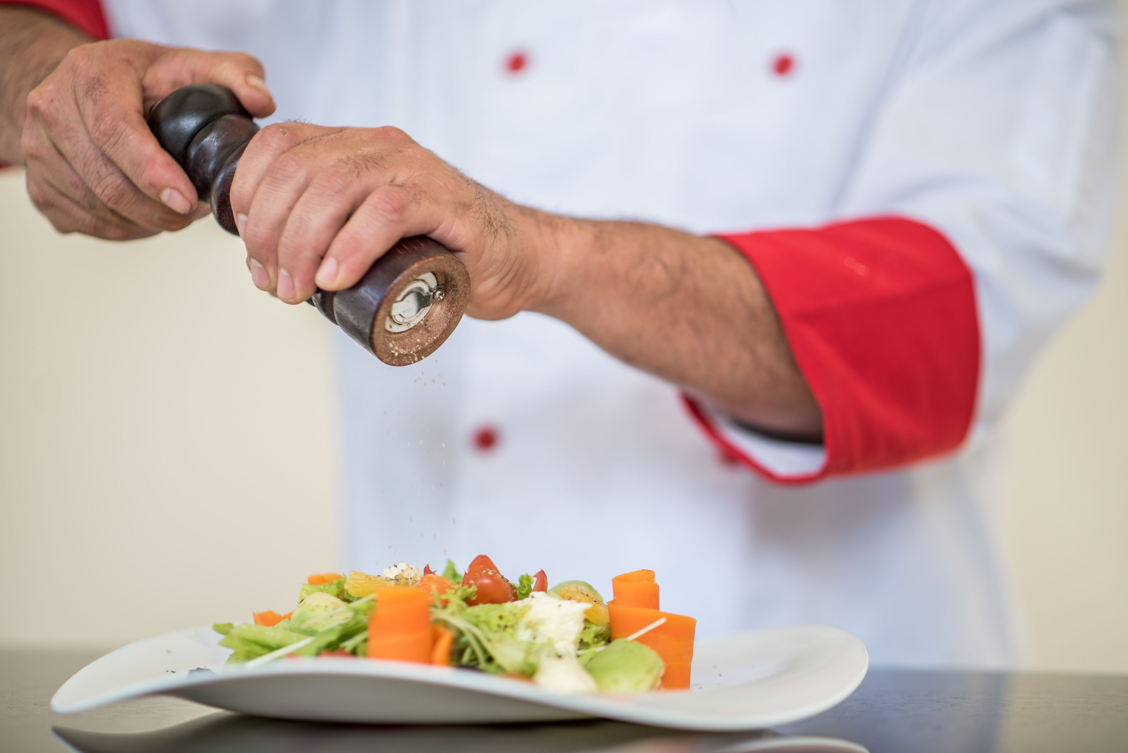 A chef seasoning a salad with a pepper grinder.