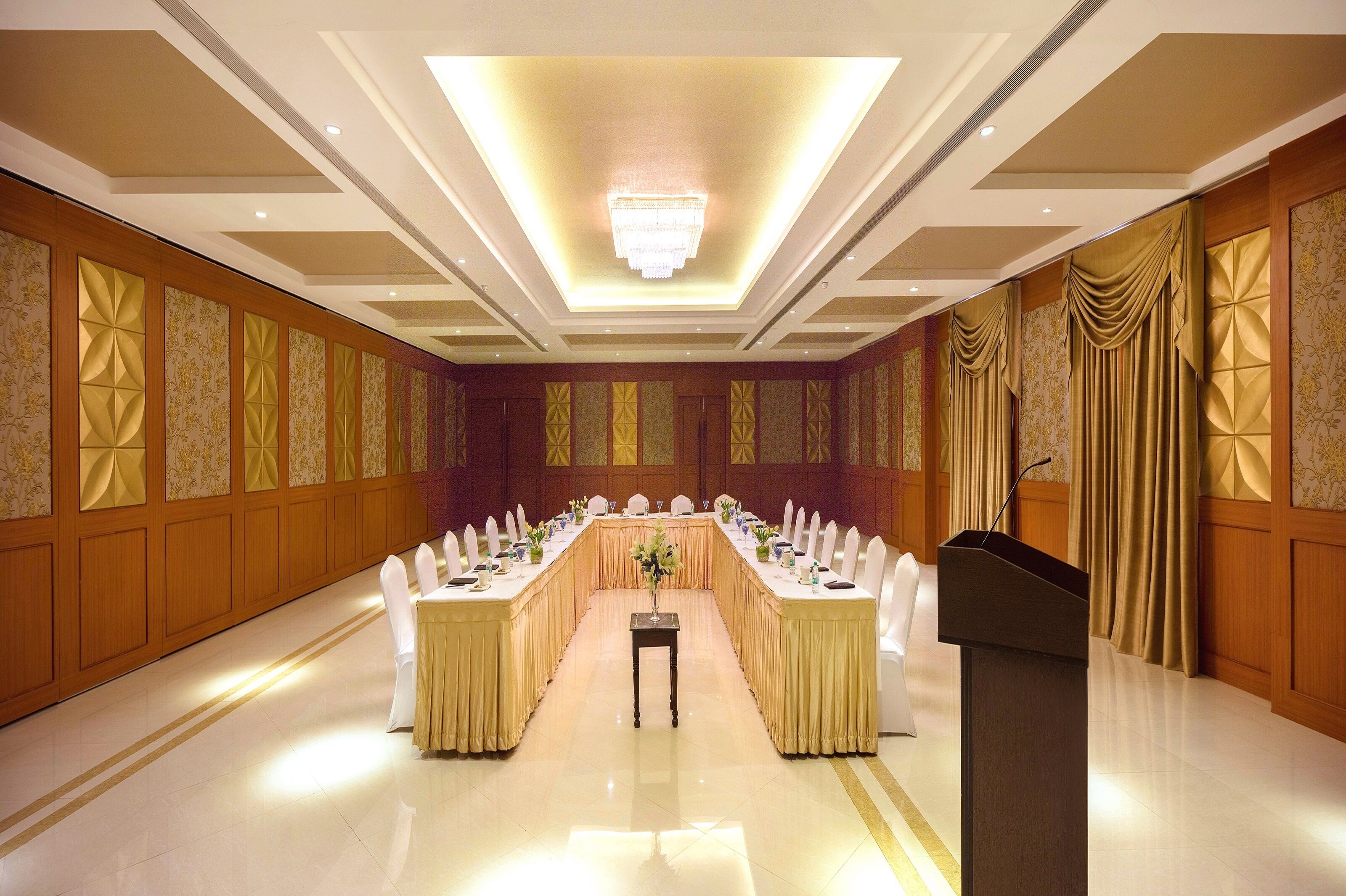 A conference room with a long table, white chairs, a podium, and a chandelier.