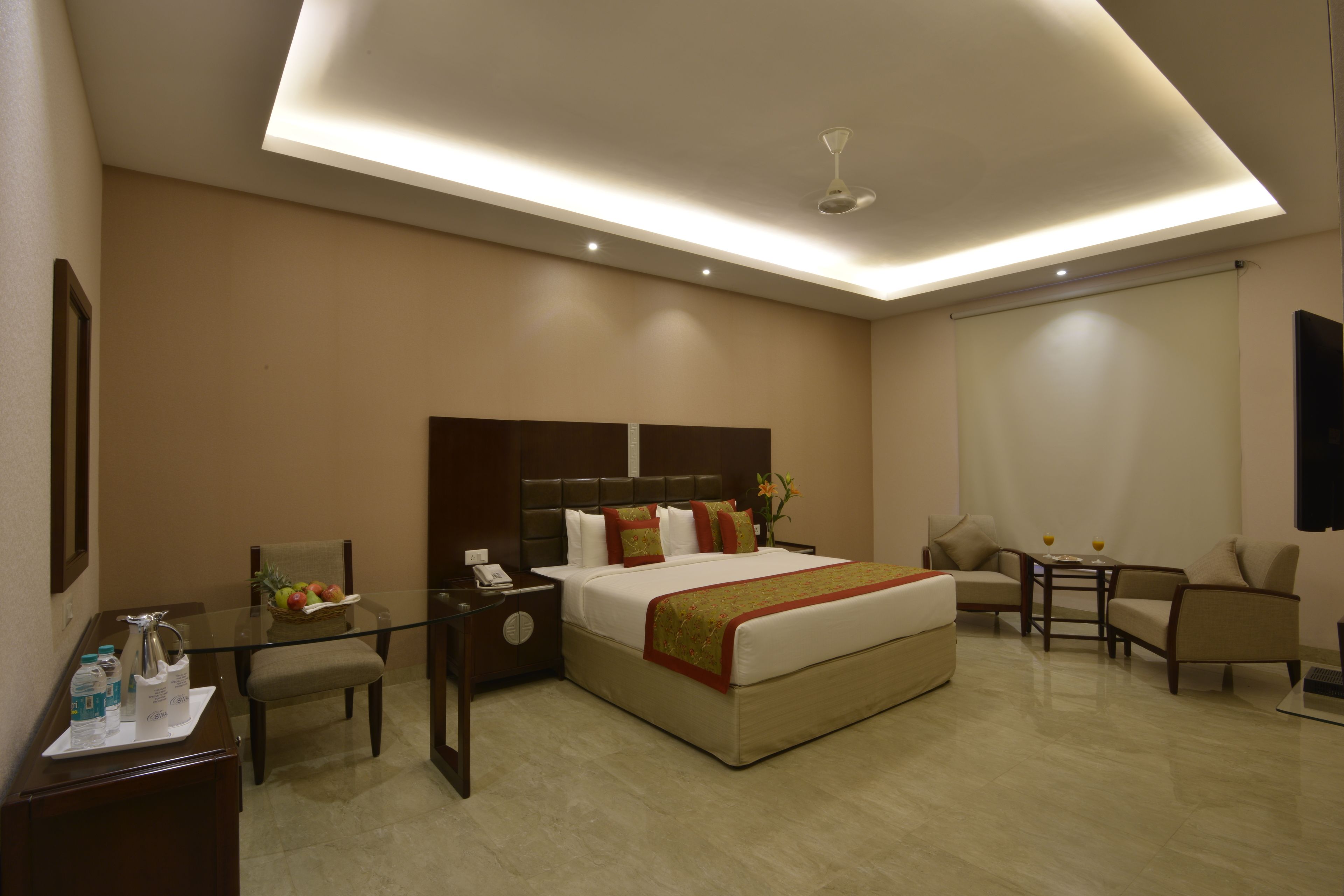 A modern hotel room with a large bed, a desk with a chair, a small table, and a sofa.