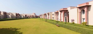 A row of modern buildings with a central dome, well-maintained lawns, and a bench. - Orchha Palace and Convention Centre (Nivari)