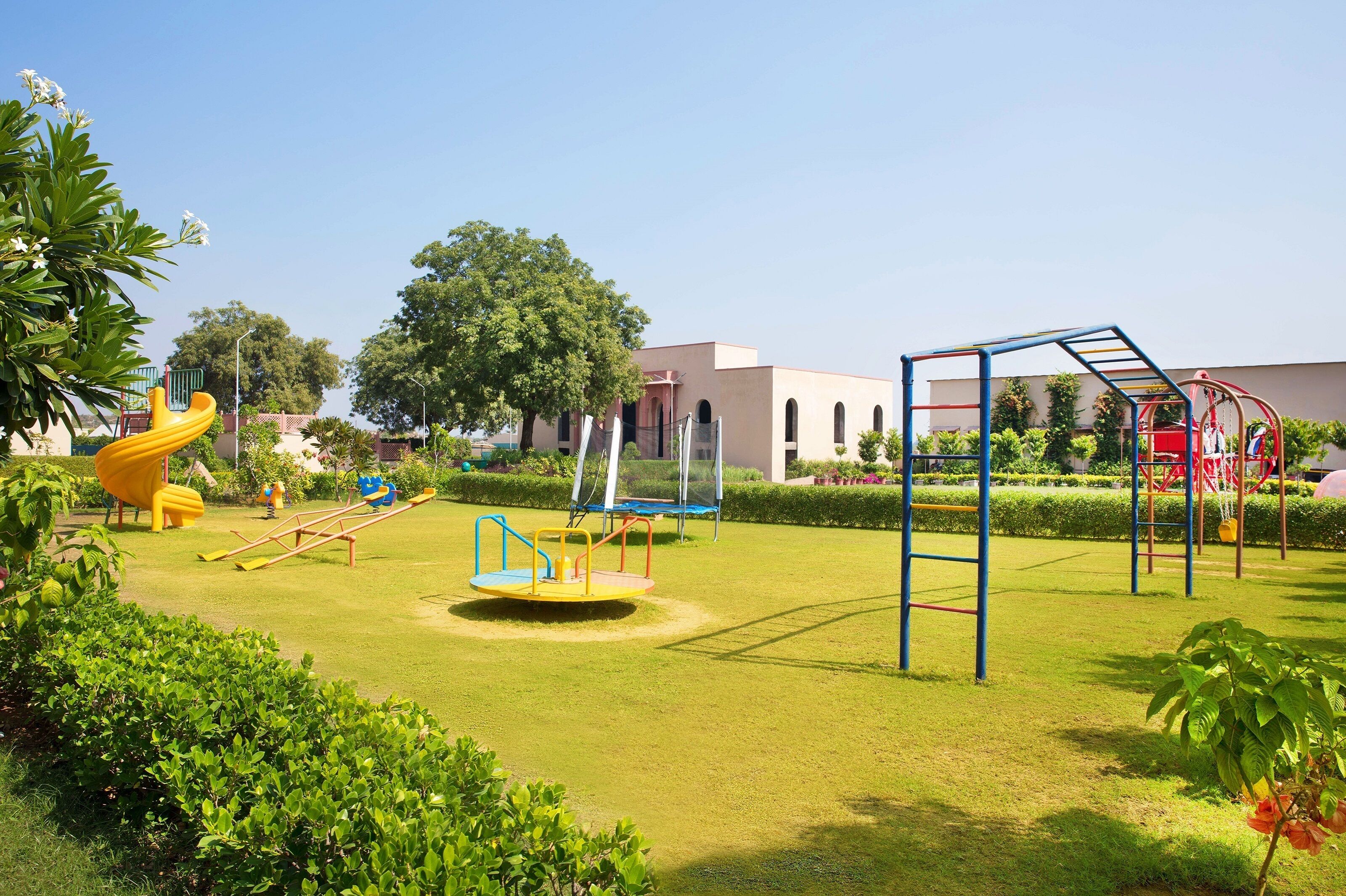 A playground with various play equipment, a building with arched windows, and well-maintained greenery.