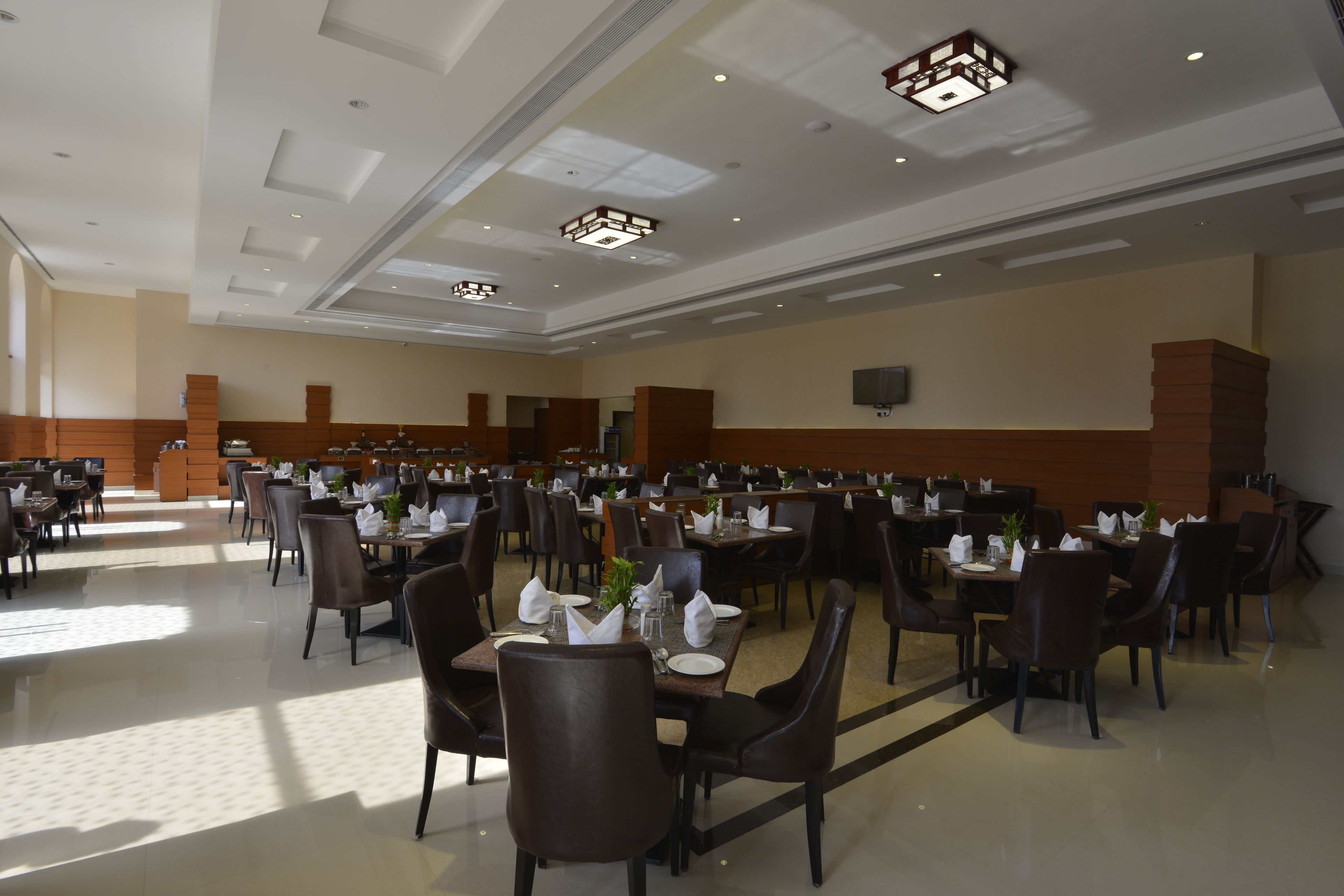 Un'ampia sala da pranzo con diversi tavoli e sedie, soffitto alto con illuminazione a incasso e colori neutri.