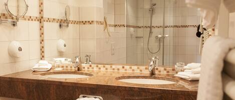 A hotel bathroom with two sinks, a mirror, a towel rack, and a shower area.