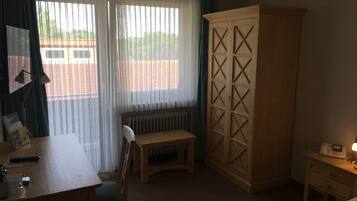 Een hotelkamer met een houten bureau, een stoel, een kast met een geometrisch patroon, een radiator en een nachtkastje met een lamp.