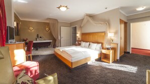 A hotel room with a large bed, a sitting area with a chair, a desk, a vanity with a mirror, and a shower area. - Hotel Backenkoehler (Ganderkesee)