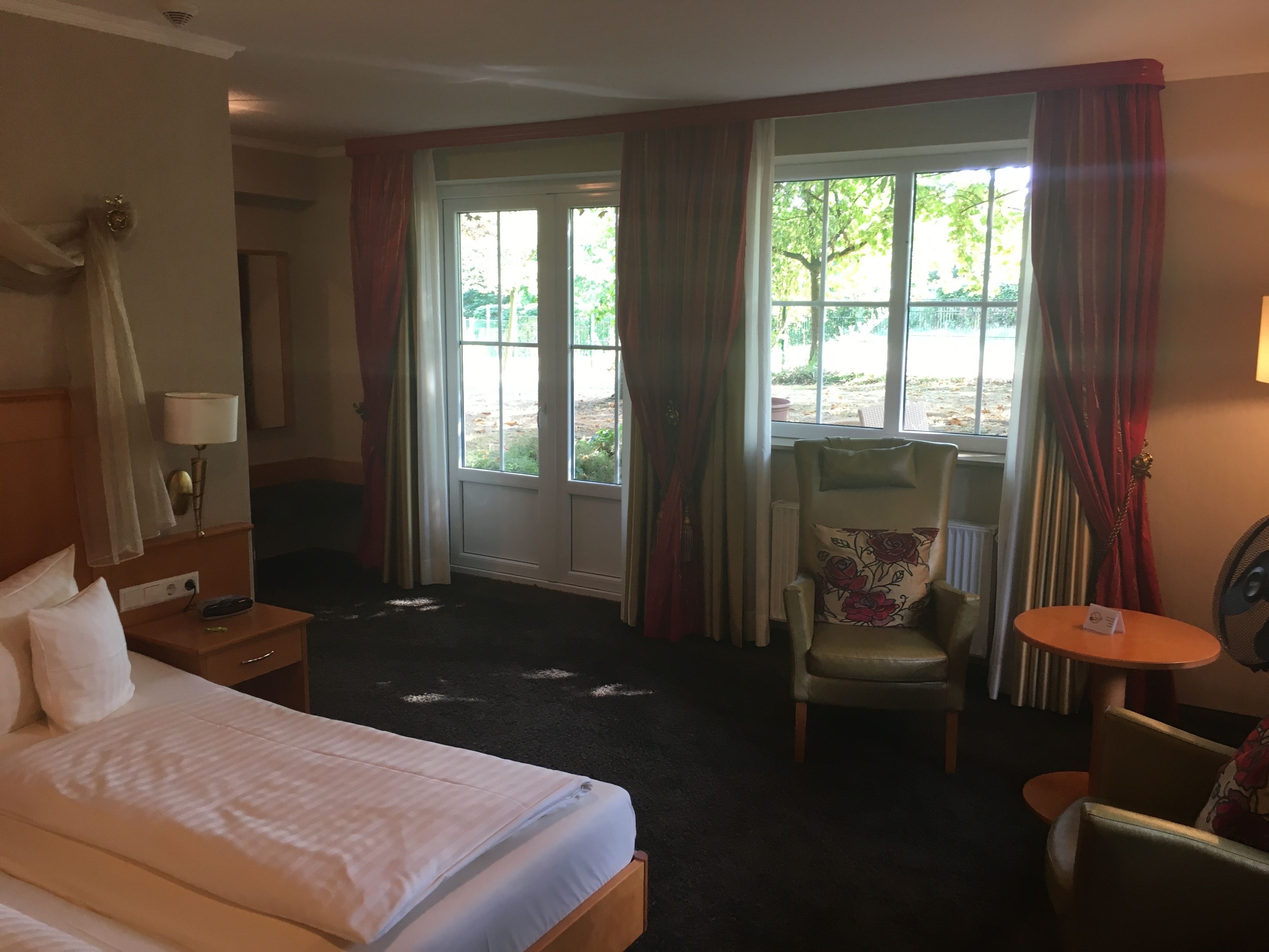 A hotel room with a bed, a chair, a small table, and a window with curtains.