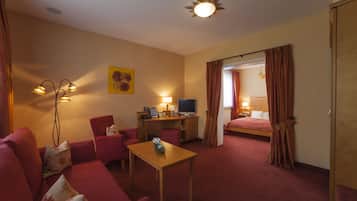 A hotel room with a red sofa, a wooden table, a desk with a computer, and a bed with curtains.