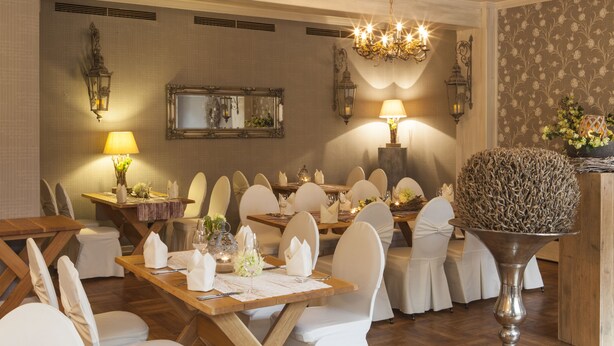 A formal dining room with wooden tables, white chairs, chandeliers, and wall-mounted sconces. - Hotel Backenkoehler (Ganderkesee)