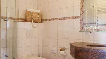A bathroom with a glass shower enclosure, a toilet, a sink with a mirror, and a trash bin.