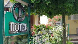 A hotel sign with a vintage design, surrounded by lush greenery and flowering plants. - Hotel Backenkoehler (Ganderkesee)