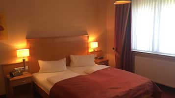 Una habitación de hotel con cama, dos lámparas de noche, una mesita de noche, teléfono y ventana con cortinas.