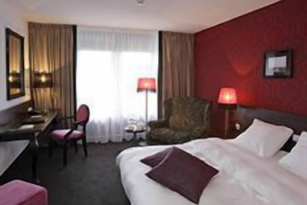 A hotel room with a bed, a desk, a chair, and a lamp.