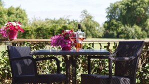 A table with two chairs, a bottle, and a glass of wine on an outdoor balcony with a view of greenery. - Hotel Mijdrecht Marickenland (Mijdrecht)
