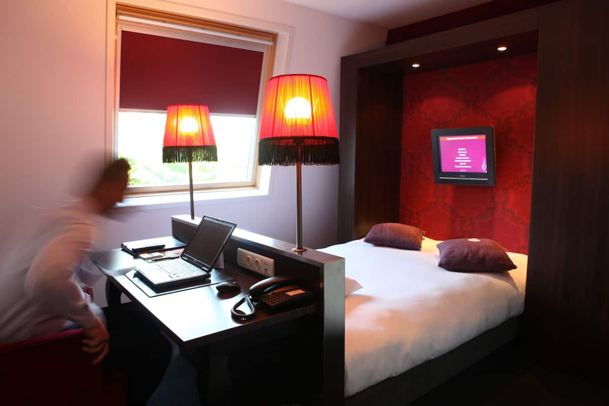 A hotel room with a desk, laptop, and telephone, a bed with pillows, and a television on the wall.