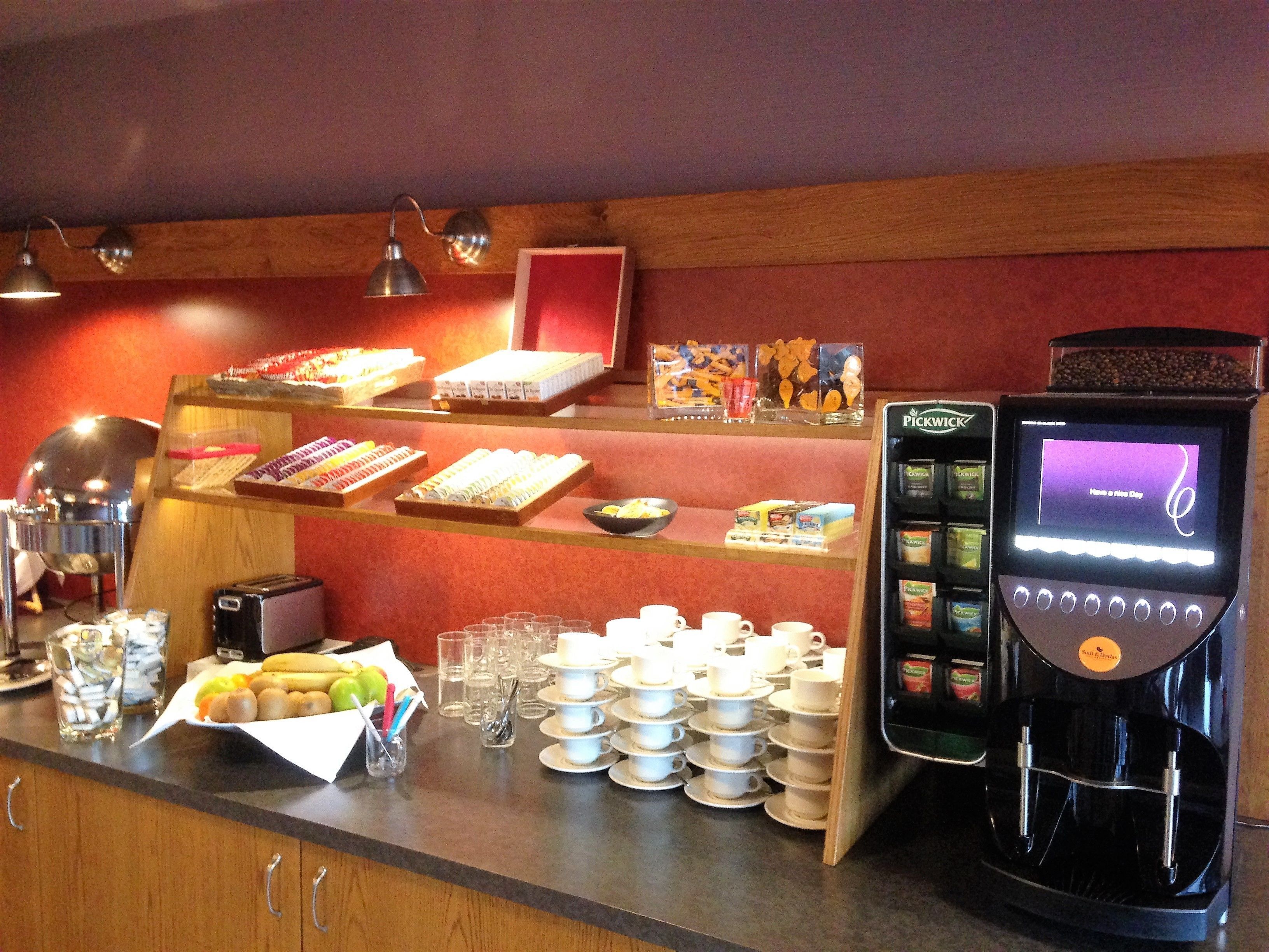 Una barra de desayuno con diversas opciones de comida, una máquina de café y un menú digital.