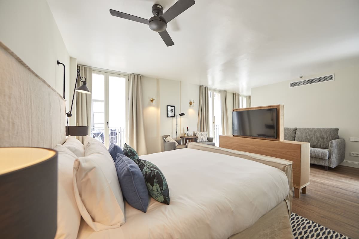 Une chambre d’hôtel moderne dotée d’un grand lit, d’un ventilateur de plafond, d’une télévision, d’un canapé et d’une fenêtre avec des rideaux.