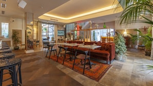 Amplia sala de estar con un sofá grande, una mesa de comedor y sillas, rodeada de plantas en macetas y una alfombra estampada.