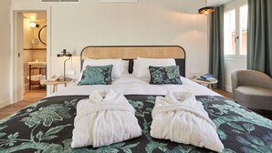 Habitación de hotel con una cama grande, dos mesitas de noche, una silla y vistas al exterior.