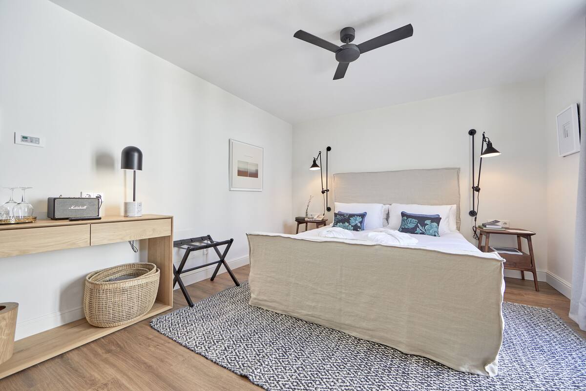 Une chambre à coucher comprenant un lit, des tables de chevet, un bureau, un ventilateur de plafond et une radio fixée au mur.