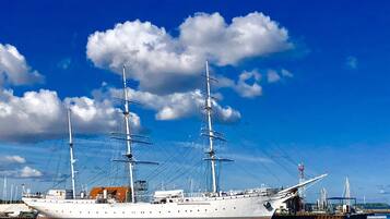 A large white ship docked at a port with a clear blue sky and clouds in the background.
