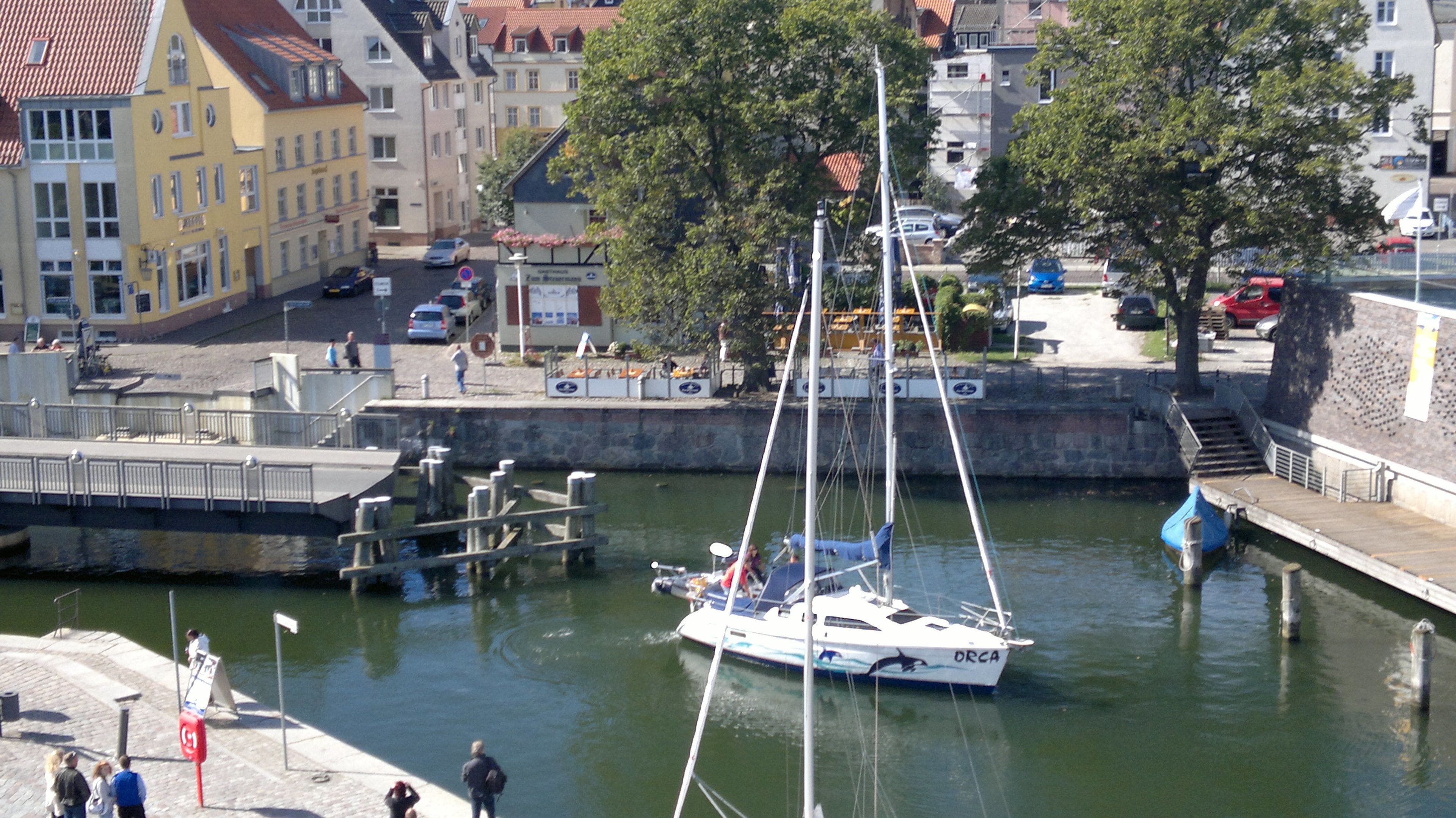 A marina with a sailboat docked, surrounded by buildings and a stone wall.