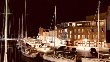 Eine Marina bei Nacht mit mehreren angestaubten Booten, ein Gebäude mit der Aufschrift 'HOTEL' und eine Brücke im Hintergrund.