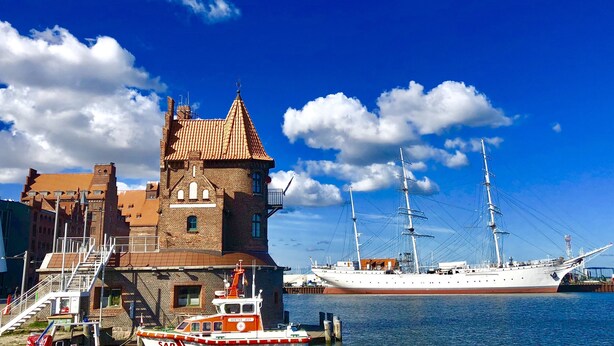 A historic building with a tower, a docked tall ship, and a small boat named "HERTHA JEFF". - Hotel Kontorhaus Stralsund (Stralsund)