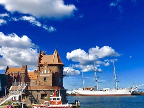 A historic building with a tower, a docked tall ship, and a small boat named "HERTHA JEFF".