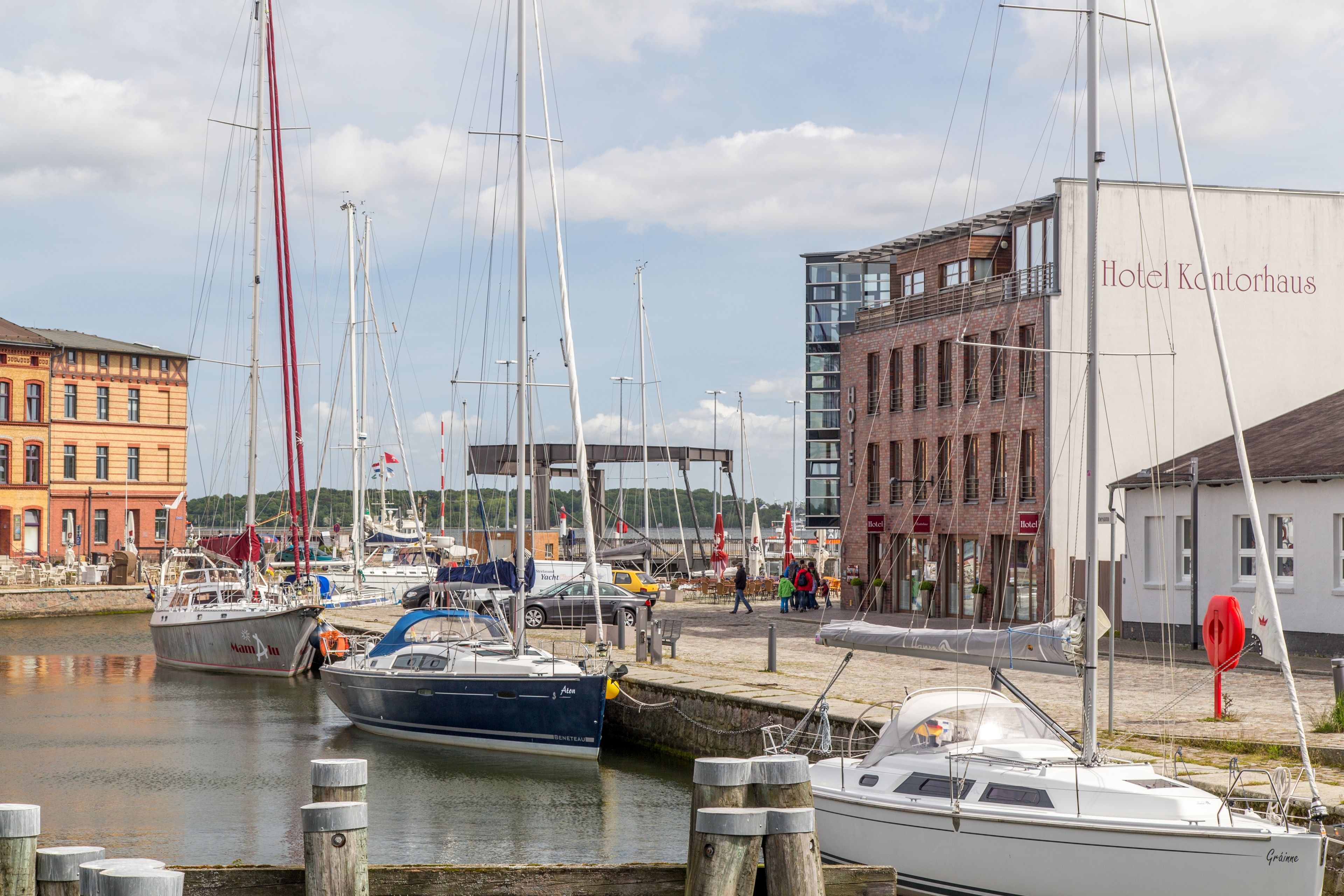 A marina with several boats docked, a modern building labeled "Hotel Kantorhaus," and a brick building in the background.