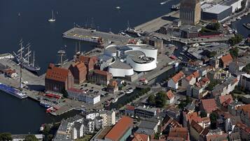 Vista aérea de un puerto con un barco grande atracado, un edificio circular con un techo distintivo y una mezcla de arquitectura tradicional y moderna.