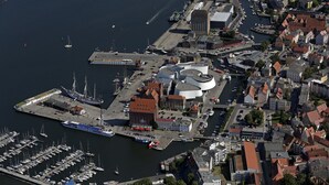 An aerial view of a marina with boats docked, a large circular building, and surrounding residential and commercial buildings. - Hotel Kontorhaus Stralsund (Stralsund)