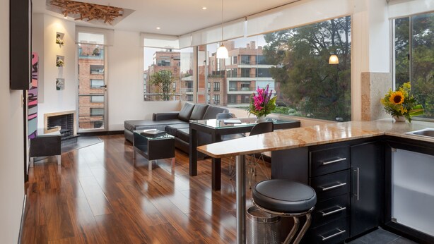 A modern kitchen with a large island, black cabinetry, and a view of the cityscape. - 104 Art Suites (Bogotá)