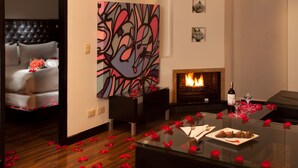 A modern living room with a fireplace, a glass coffee table with rose petals, and a large abstract painting on the wall. - 104 Art Suites (Bogotá)