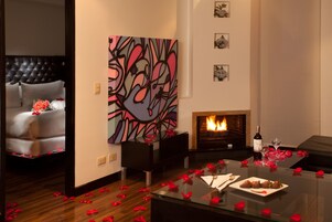 Una sala de estar moderna con chimenea, una mesa de centro de vidrio con pétalos de rosa y un cuadro abstracto grande en la pared.