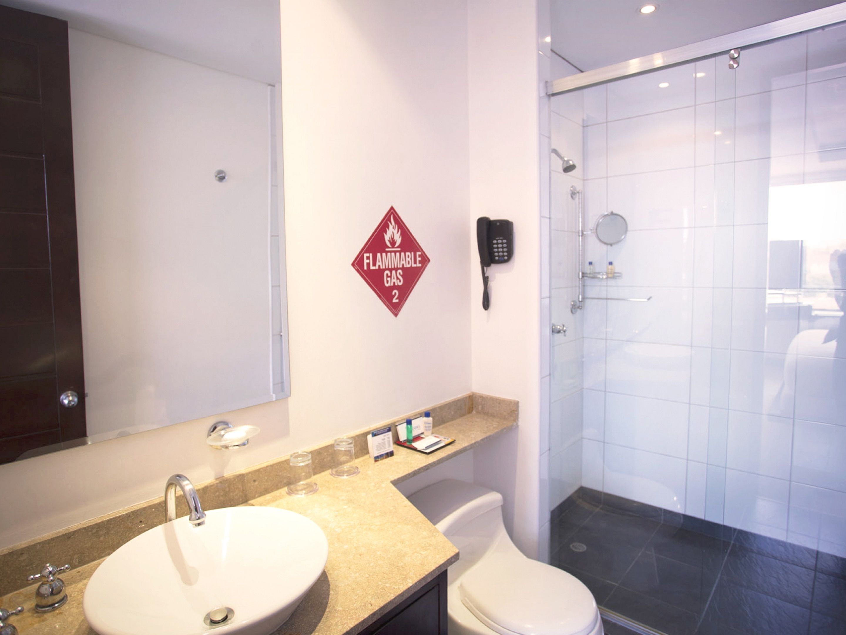 Un baño con lavamanos, inodoro y ducha. Hay un cartel de extintor en la pared.