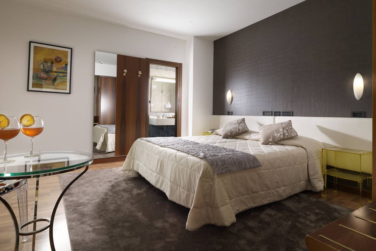 A modern bedroom with a large bed, a glass table with drinks, and a dark accent wall.