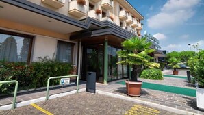A hotel with a modern facade, a covered entrance, and a green outdoor area with potted plants.