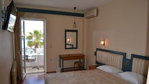 A hotel room with a bed, a desk, a chair, a television, and a balcony with a view of palm trees.