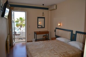 Habitació d'hotel amb llit, escriptori, cadira, televisió i un balcó amb vista a palmeres.