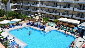 A hotel with a large swimming pool surrounded by lounge chairs and umbrellas.