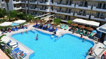 A hotel with a large swimming pool surrounded by lounge chairs and umbrellas.