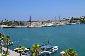 A marina with boats docked, a stone wall, and palm trees.
