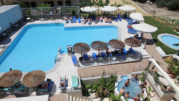 A large outdoor swimming pool with lounge chairs and umbrellas, surrounded by a landscaped area with palm trees.