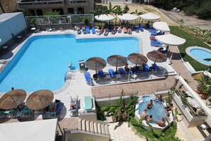 A large outdoor swimming pool with lounge chairs and umbrellas, surrounded by a landscaped area with palm trees.